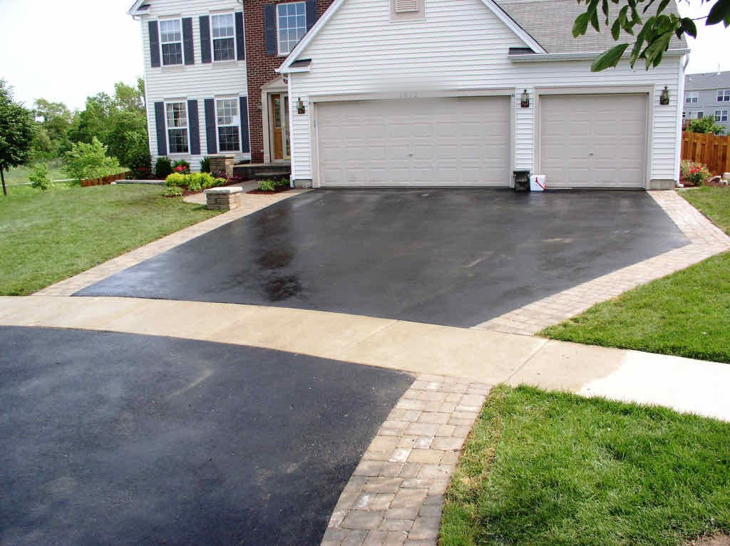 Asphalt driveway with a paver border and concrete apron leading to a three-car garage