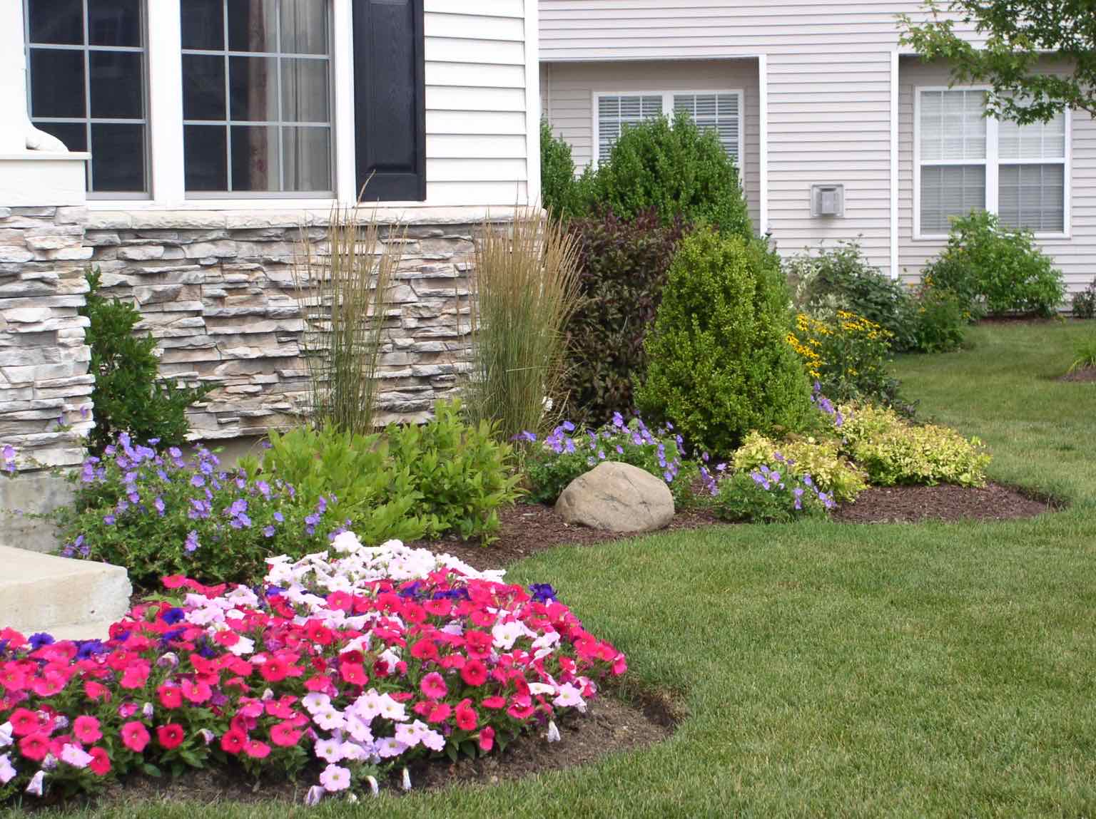 Front yard planting bed with flowers and ornamental shrubs by a stone porch