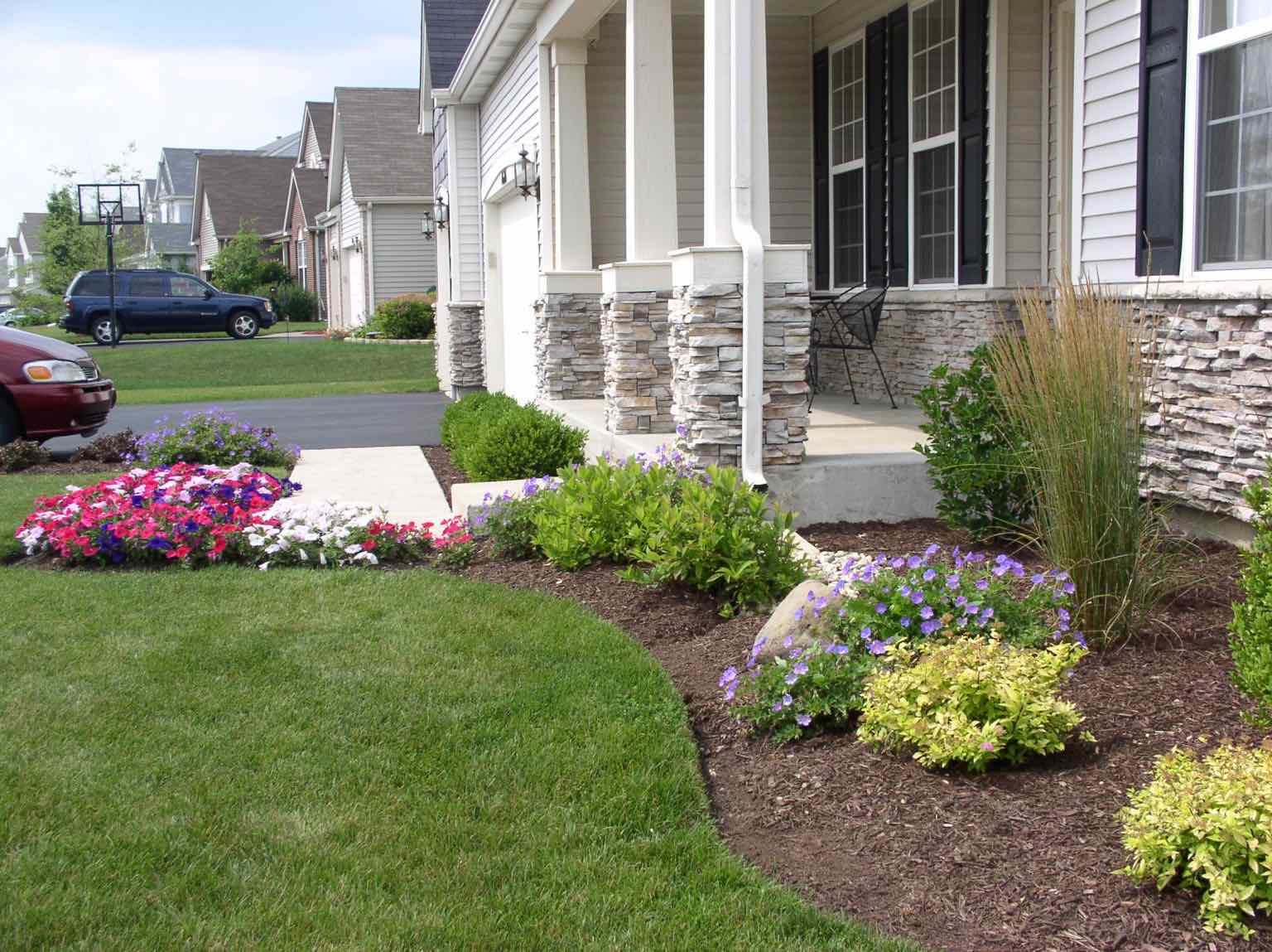 Front yard planting bed with flowers and ornamental grasses by a stone entry