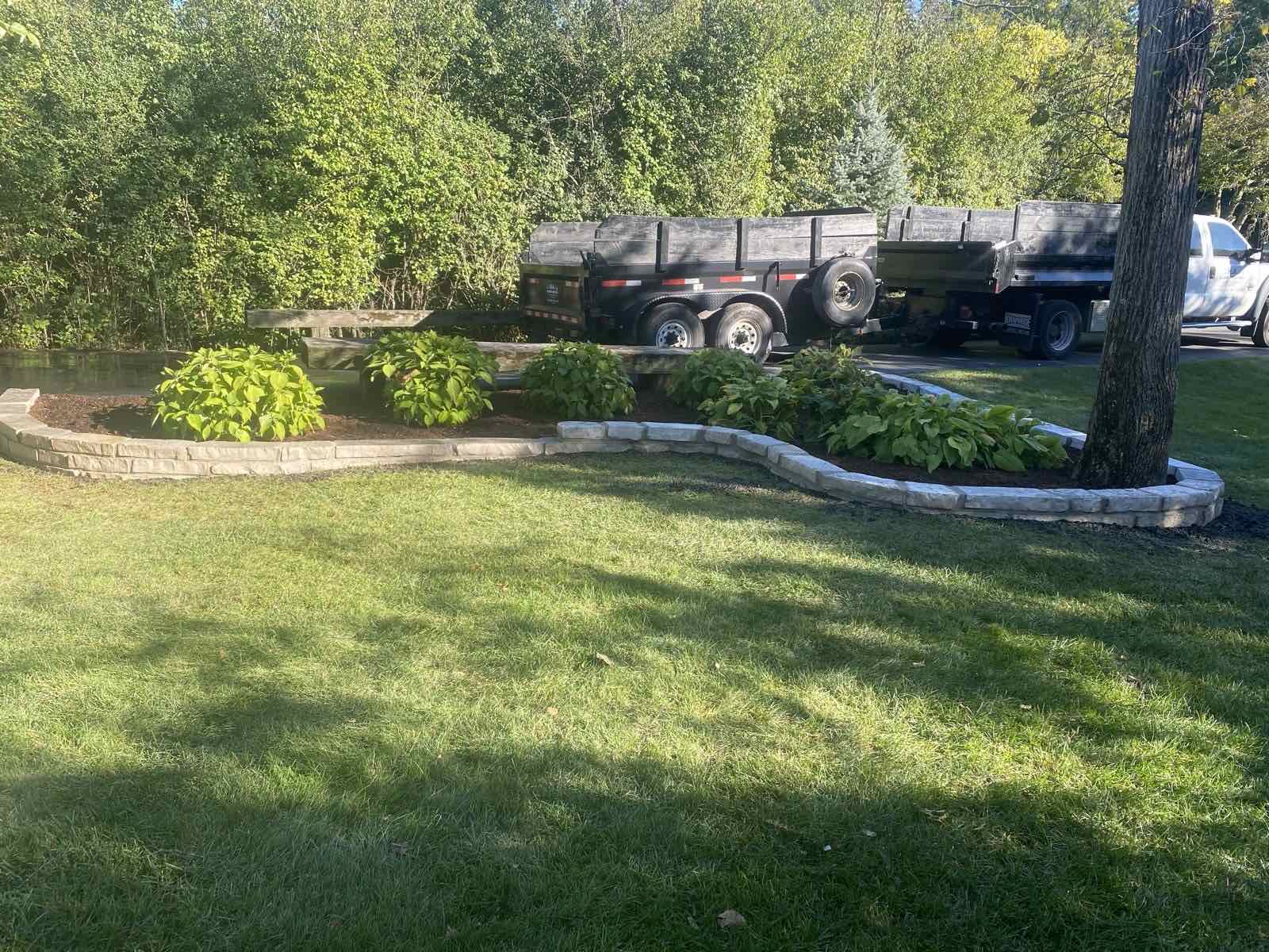 Newly built low stone wall around a freshly mulched planting bed with hostas