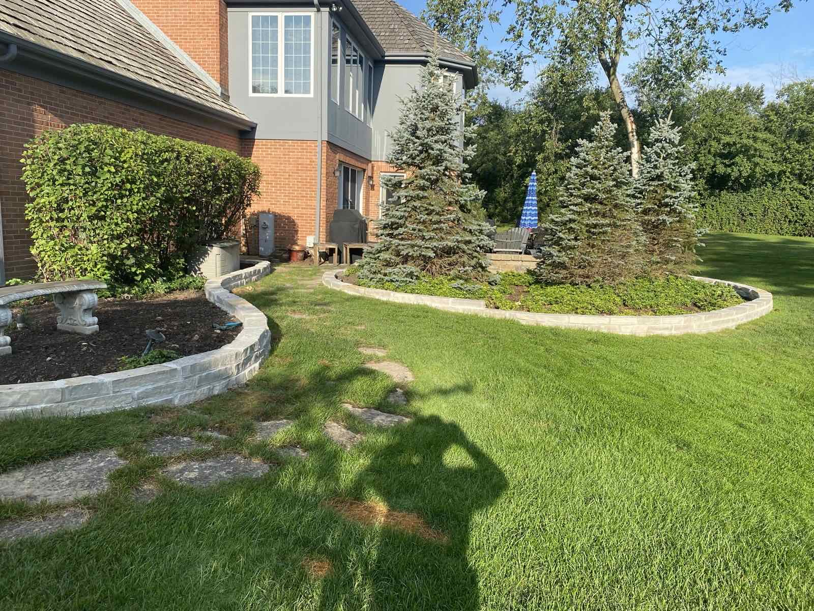 Curved stone garden walls bordering evergreen trees in a backyard planting bed