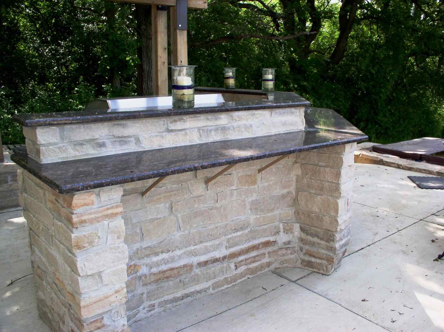 Stone outdoor bar with dark granite countertop overhang