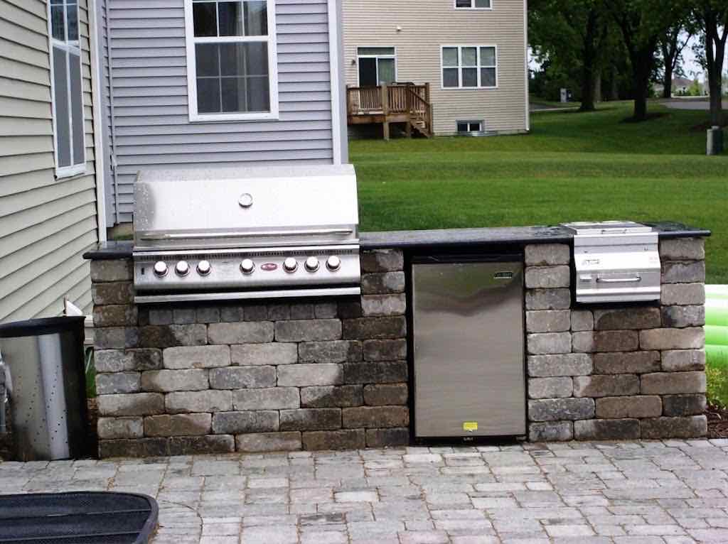 Built-in grill and mini fridge in a stone outdoor kitchen counter