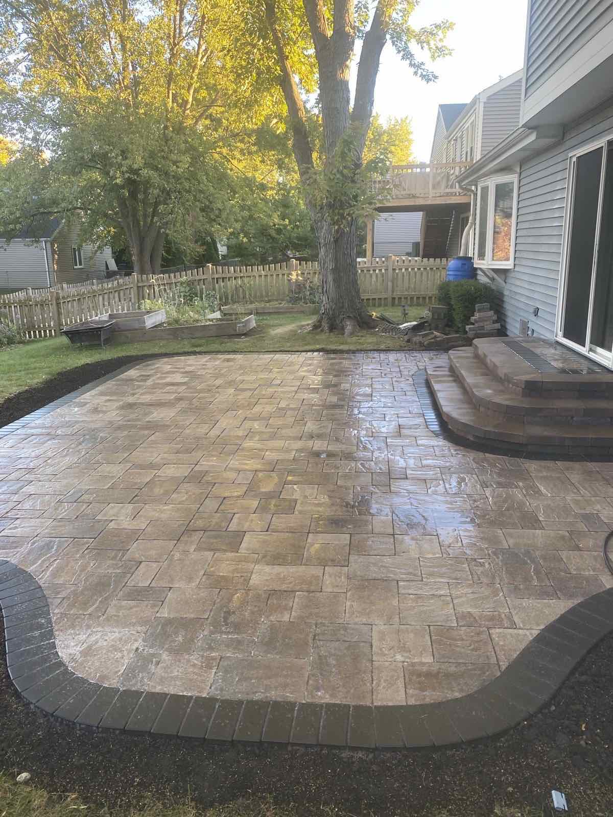 Paver patio with a curved charcoal border and stone steps up to a backyard deck