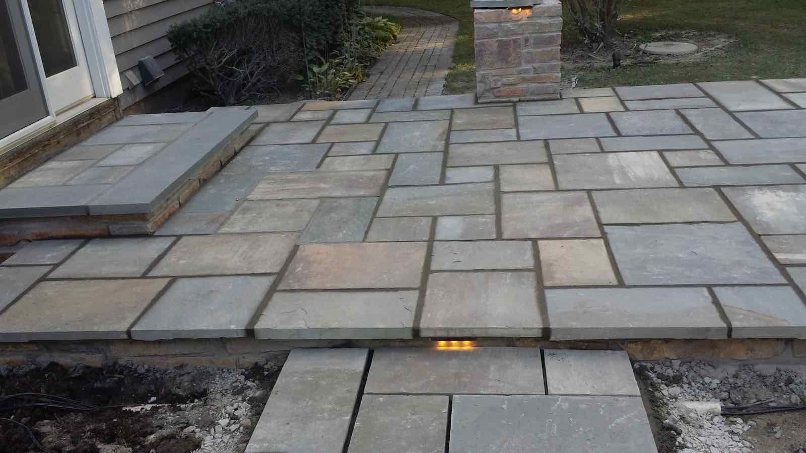 Bluestone patio with built-in step lighting and a lit stone pillar at dusk