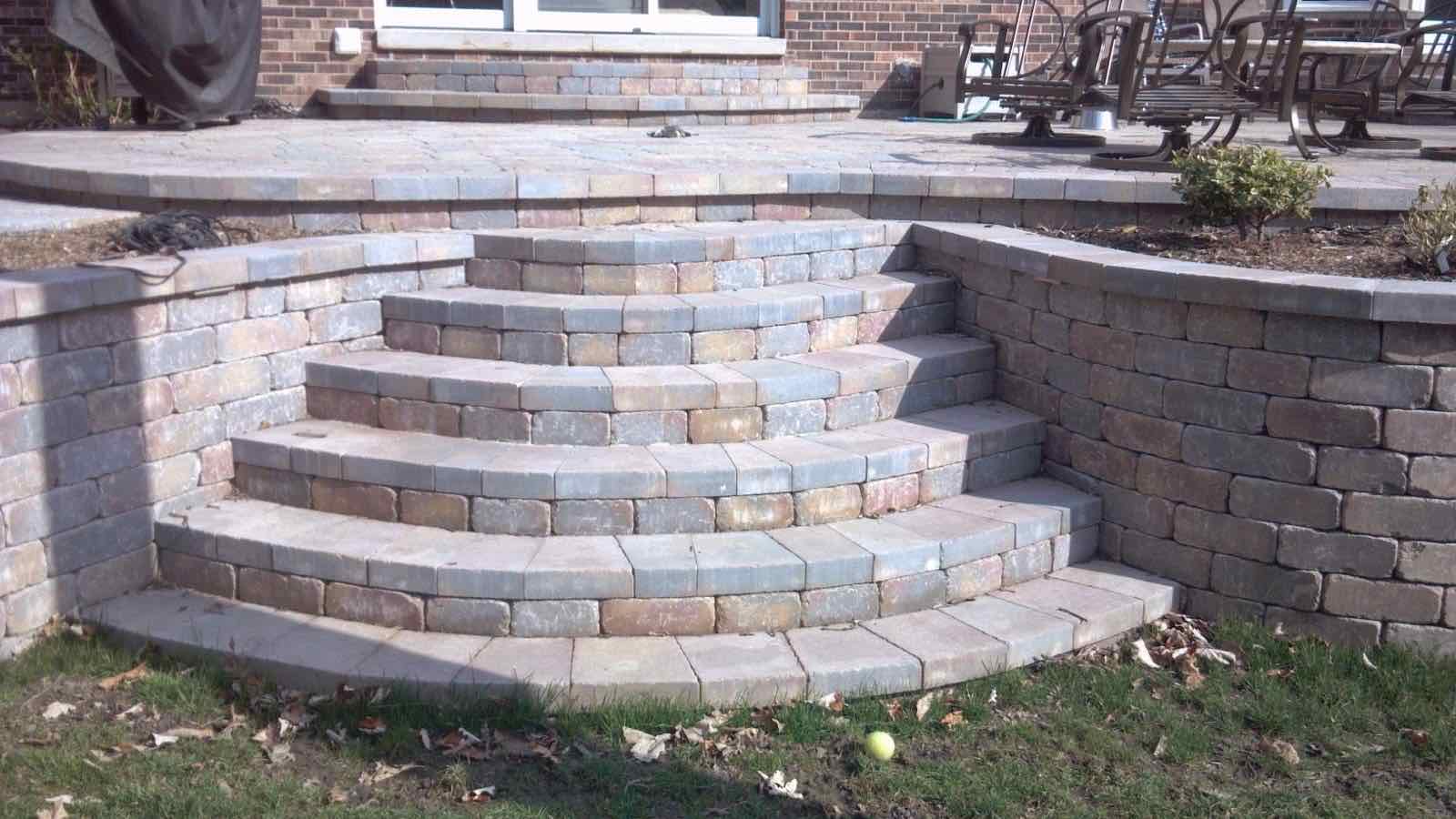 Raised paver patio with curved steps down to the yard, flanked by matching retaining walls