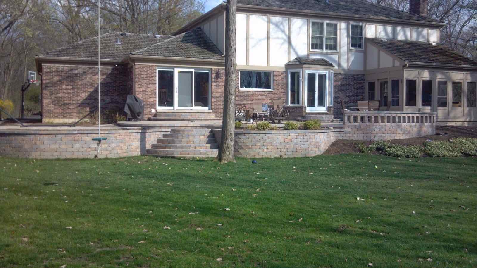 Wide view of a raised paver patio and retaining wall spanning the back of a home