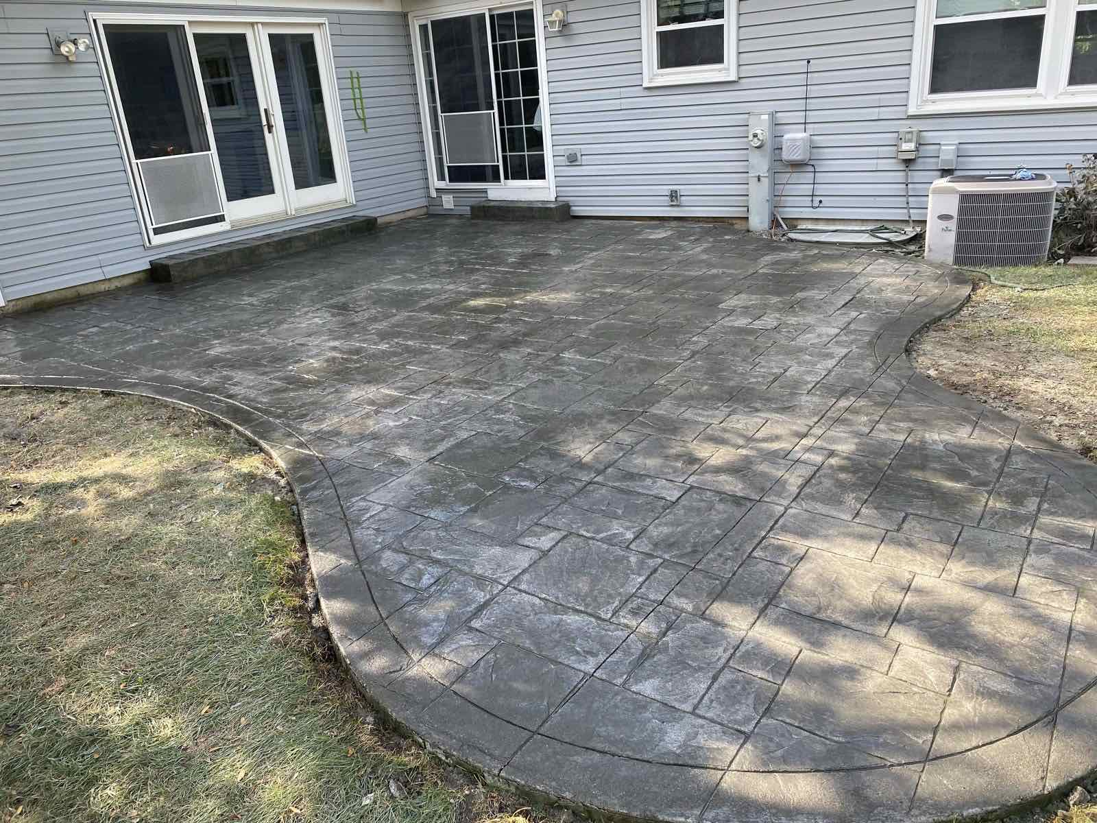 Stamped concrete patio spanning a backyard behind a two-story home