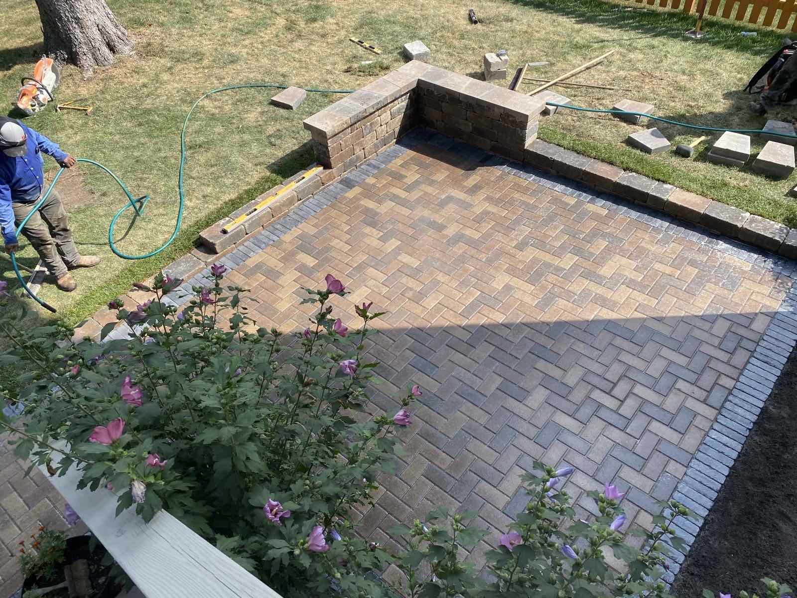 Herringbone paver patio under construction with a low seat wall