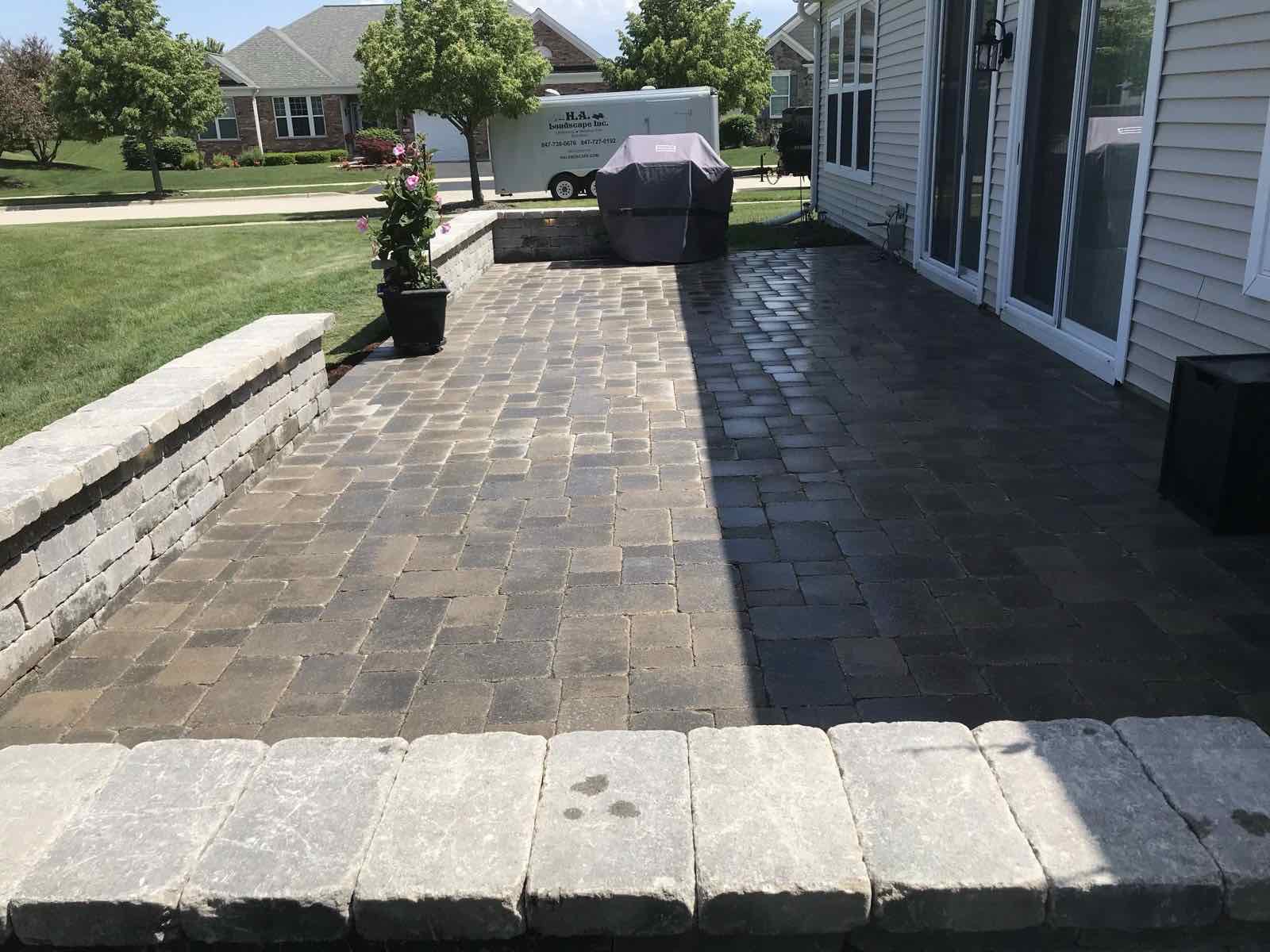 Paver patio with a stone seat wall beside a home, H.A. Landscape work trailer parked in the driveway