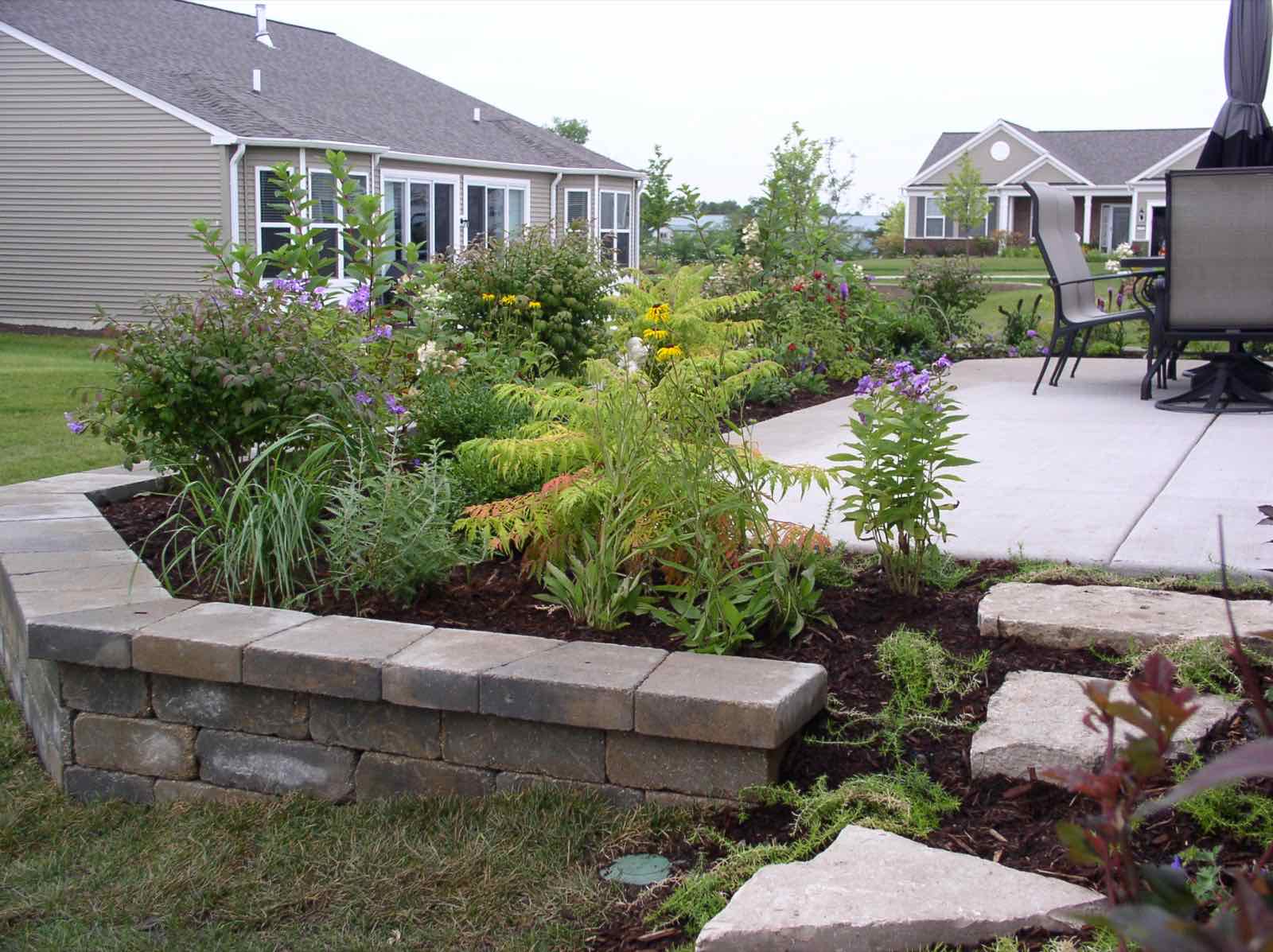 Concrete patio bordered by a stone retaining wall and garden bed
