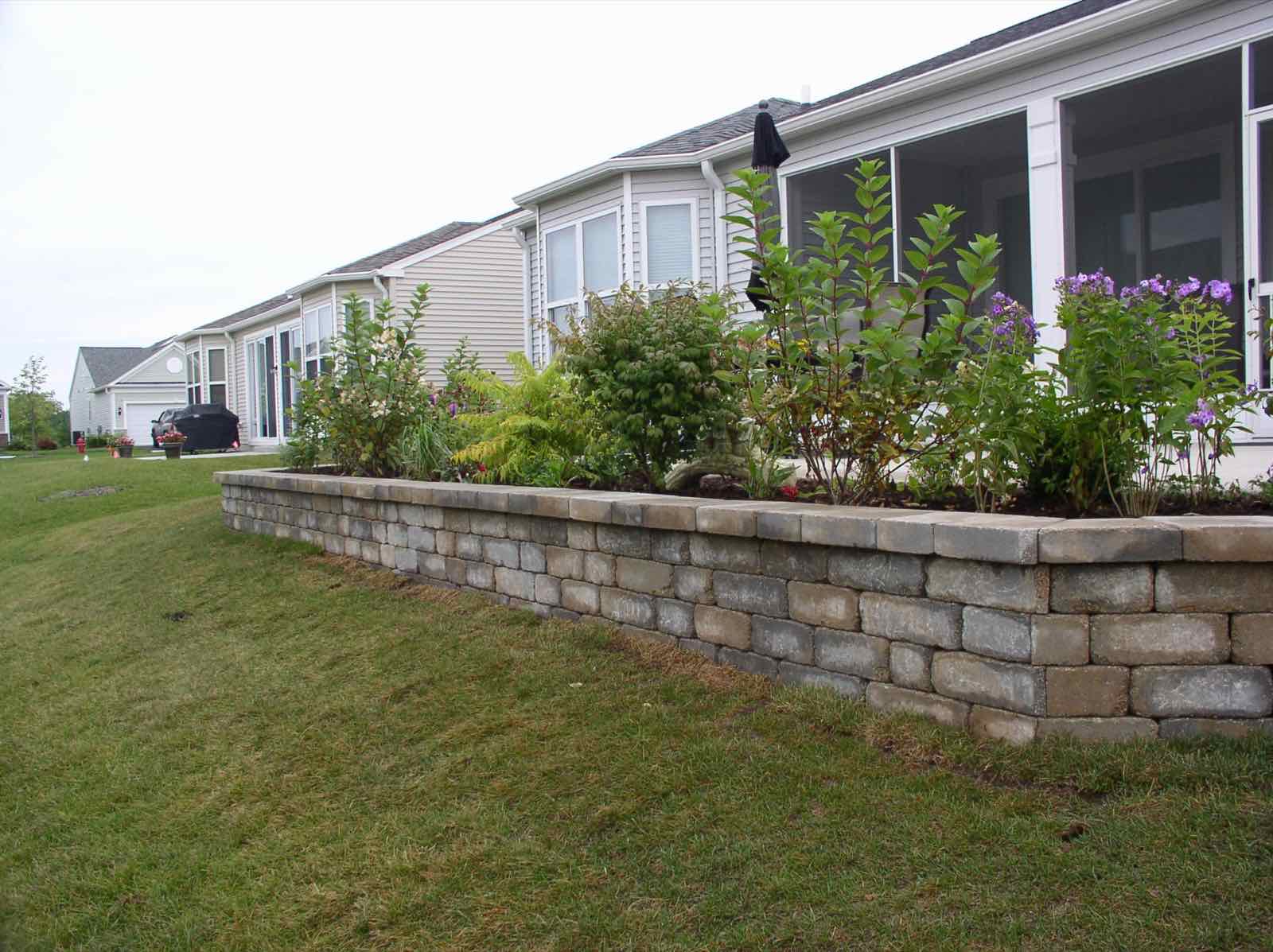 Stone retaining wall bordering a garden bed along a patio walkway
