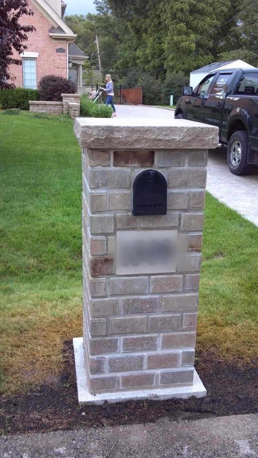 Stone-veneer mailbox pillar with a house number plaque along a driveway