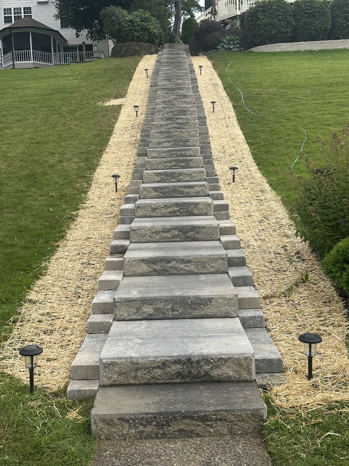 Long run of stacked block steps climbing a lawn slope, lined with path lights