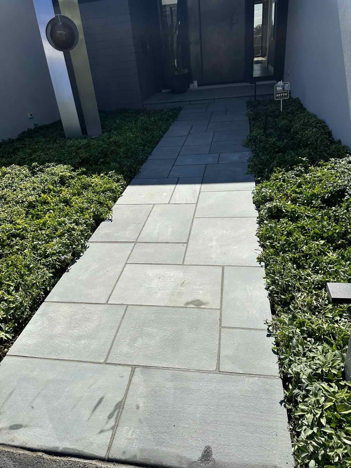 Bluestone walkway bordered by manicured hedges leading to a modern front entry