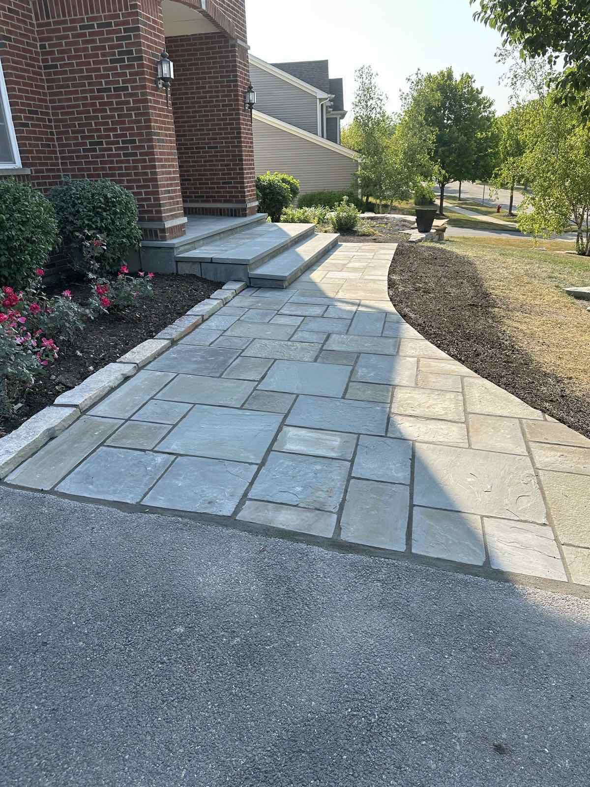 Bluestone walkway and entry steps bordered by rose bushes and a low stone wall